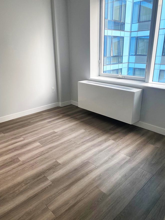 An empty bedroom with a clean floor, window and radiator cover